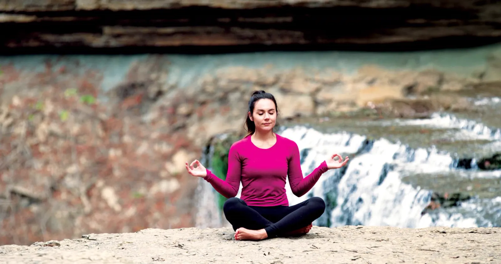 Woman practicing meditation beside a peaceful waterfall